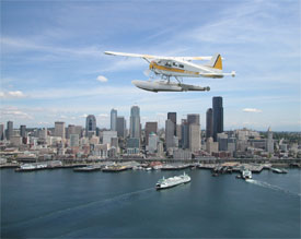 Seaplane flys over harbor and office buildings